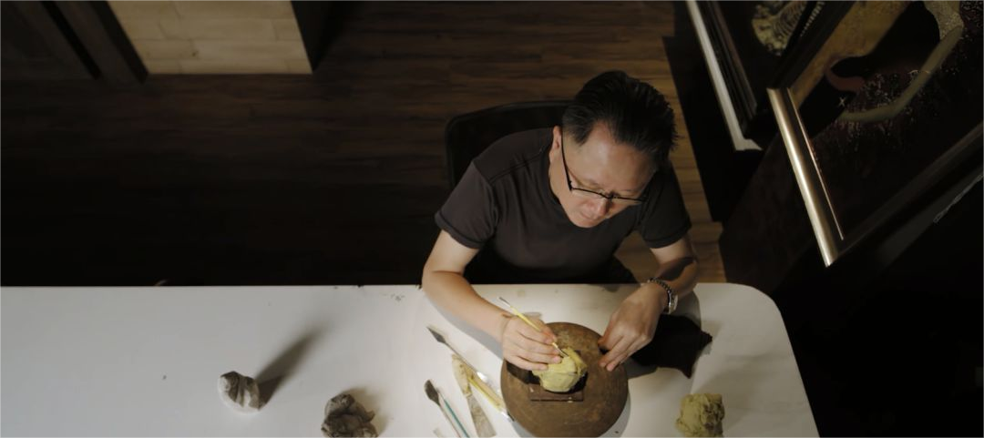 俯拍黄宝庆在工作台前观察石材并勾勒造型